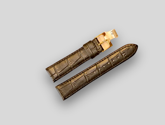 Brown crocodile-patterned watch strap with gold clasp on a light gray background