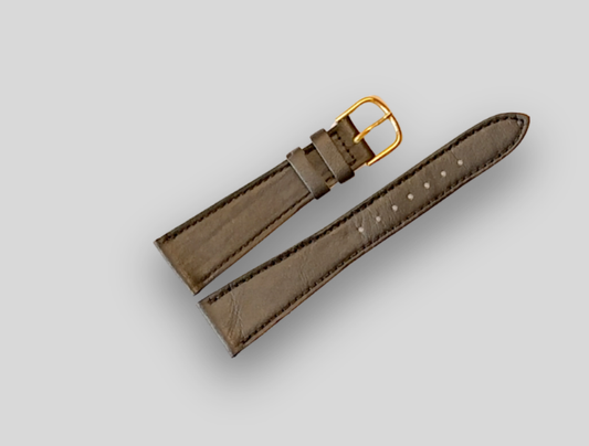 Brown leather watch strap with gold buckle on a light gray background