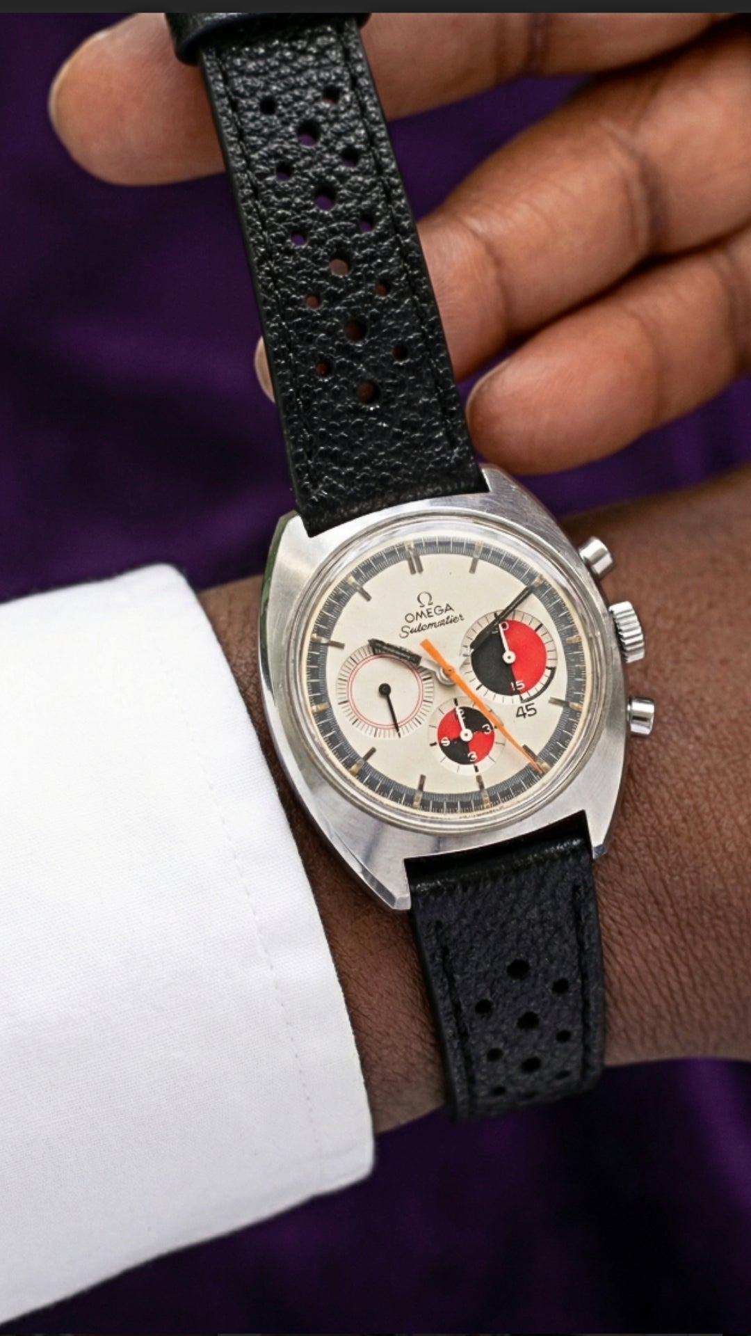 Close-up of a wrist wearing a vintage Omega watch with a black Watchmania CORFAM strap against a blurred background